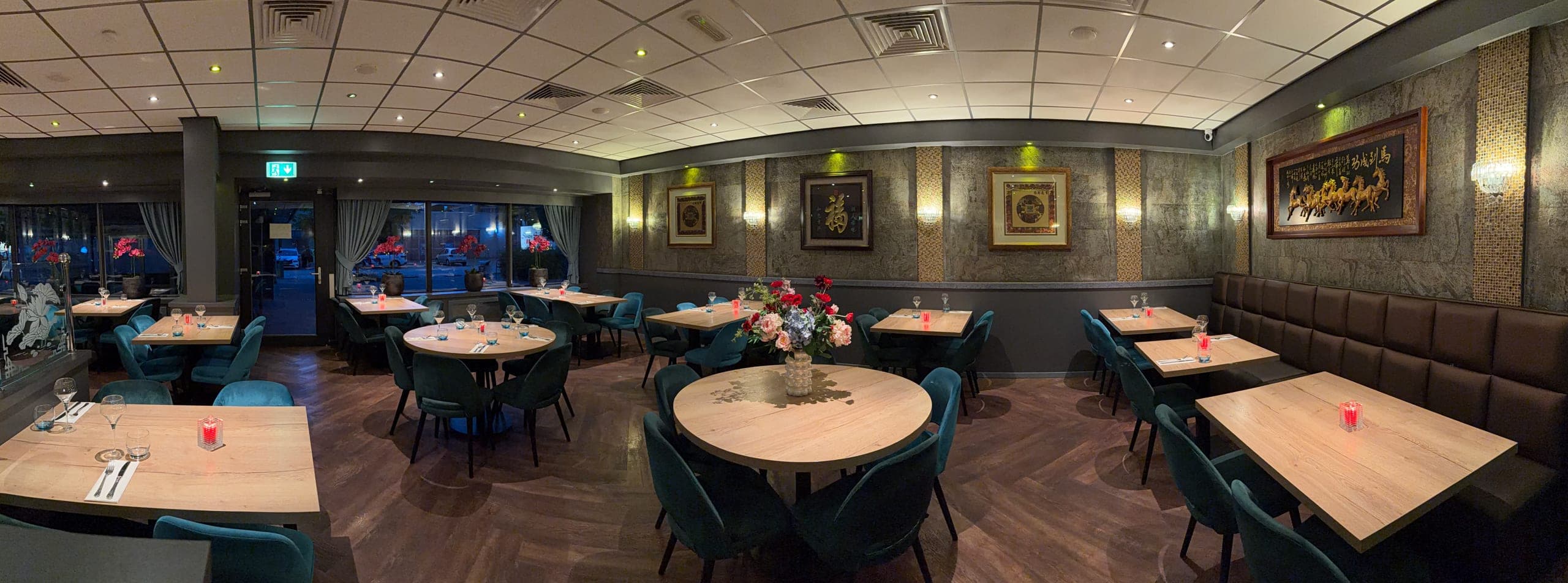 De eetzaal met ronde en vierkante tafels, blauwgroene fauteuils en Chinese kalligrafie in gouden lijsten aan de wand